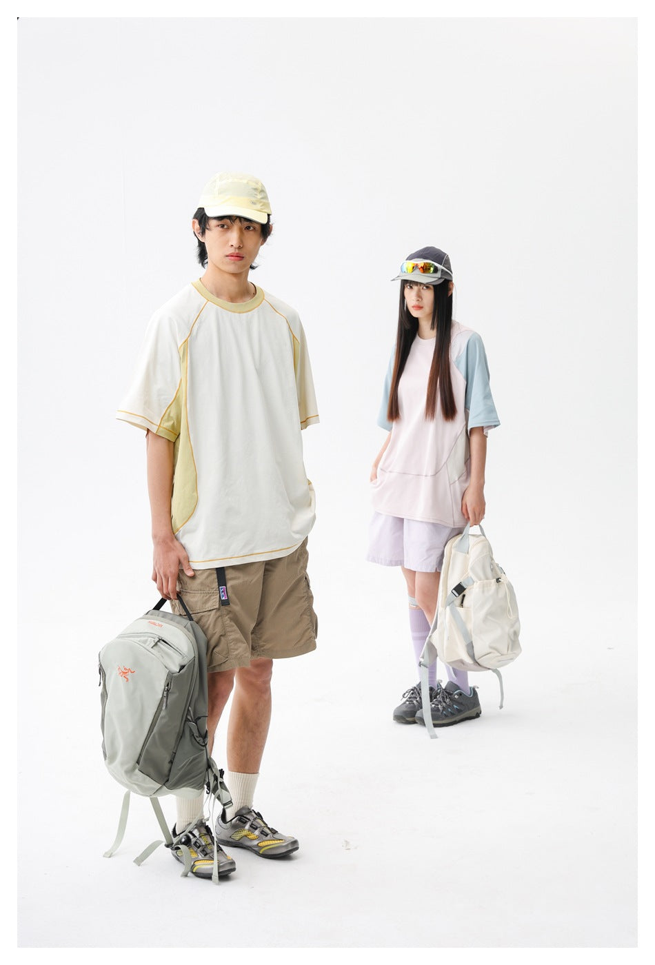 Two models wearing color-block athletic T-shirts, shorts, caps, and hiking backpacks in a white studio.