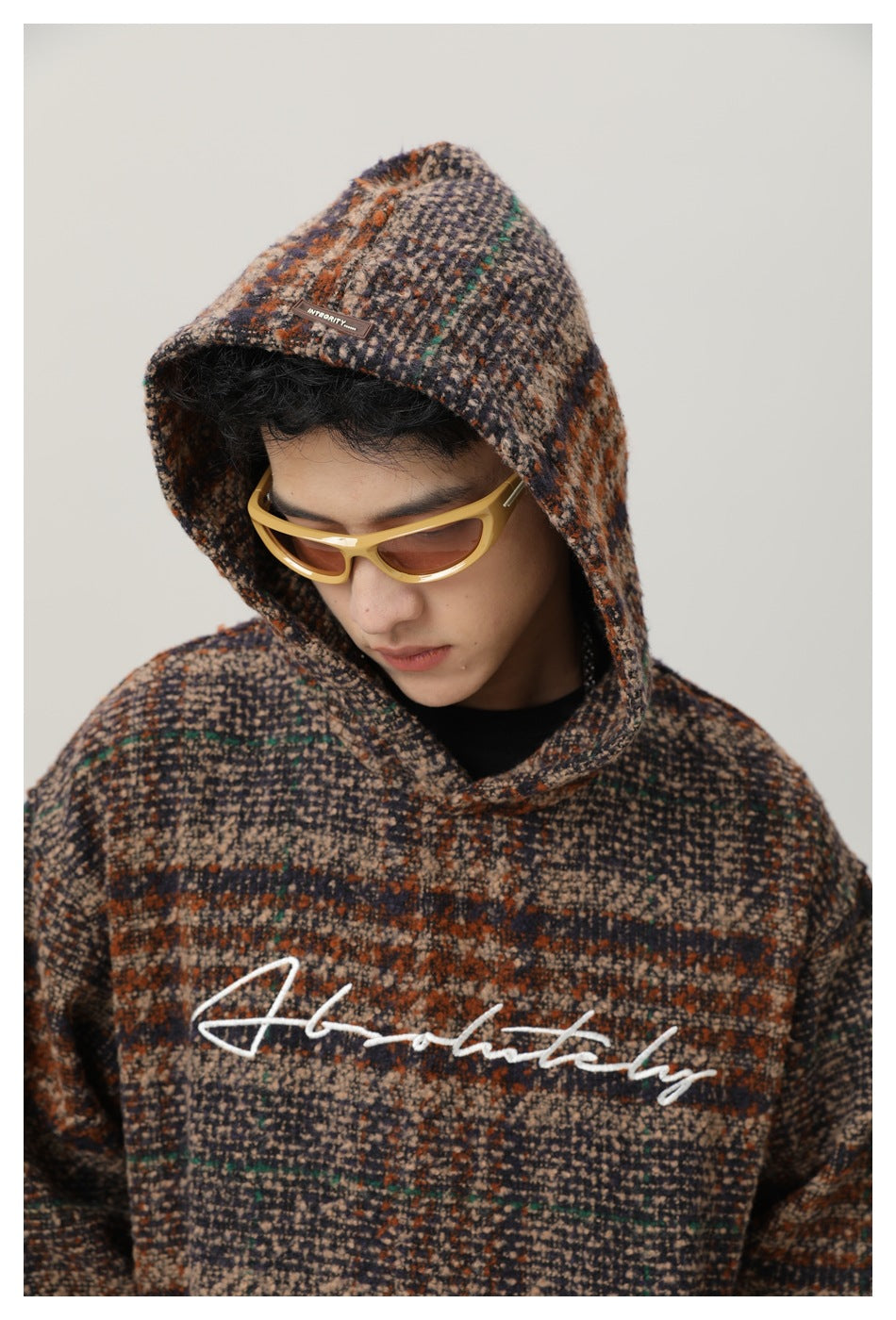 Model wearing the plaid hooded pullover with the hood up and white script across the chest.