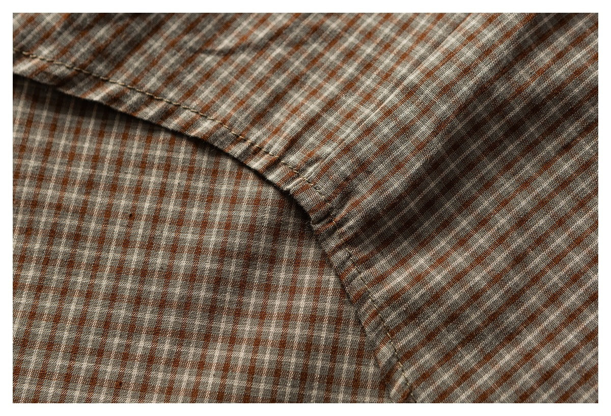 Close-up of a curved seam joining sections of rust, gray, and white checked shirt fabric.