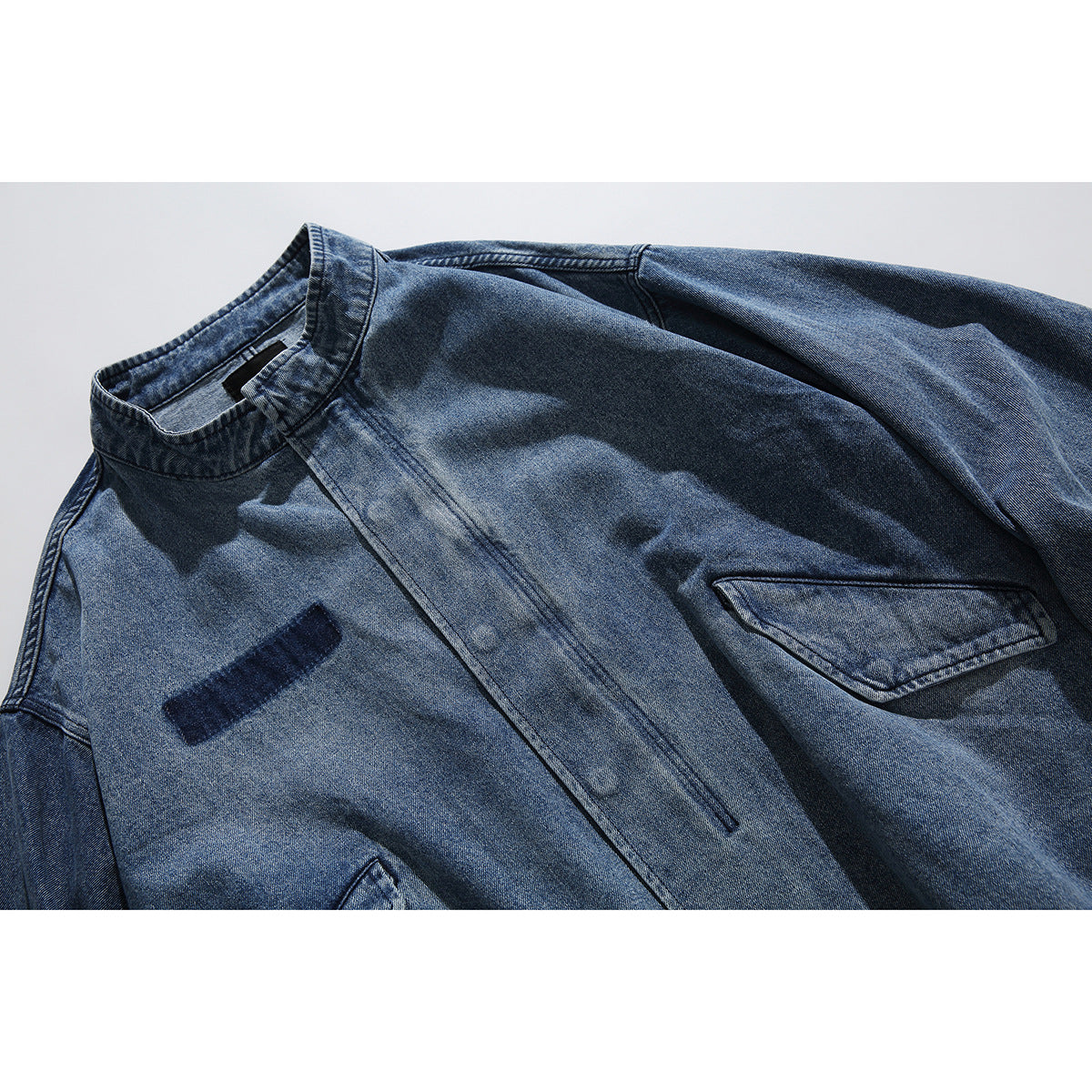 Close-up of a washed blue denim jacket showing its stand collar, front placket and flap pocket.