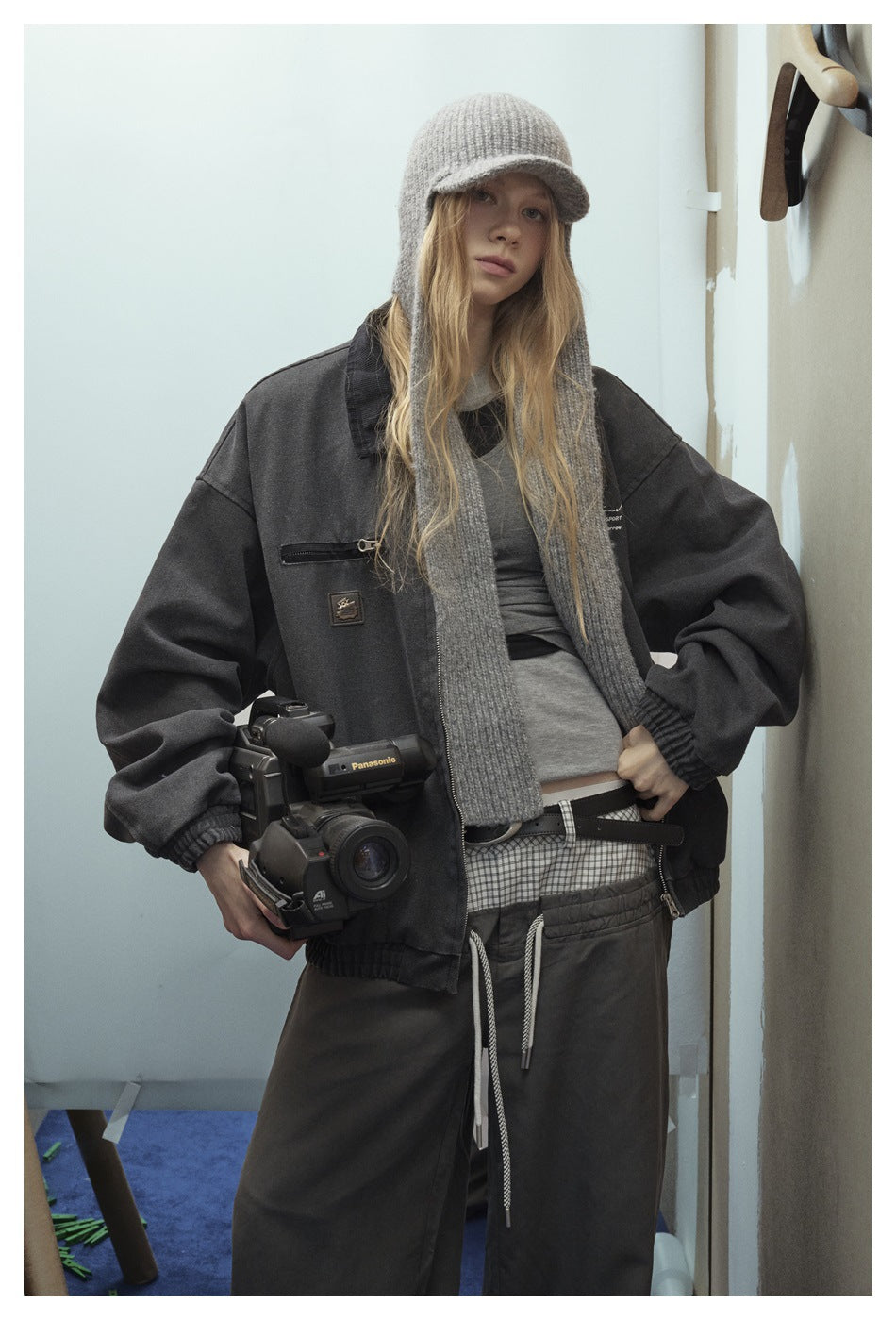 Model wearing an open charcoal jacket over a gray top, with wide-leg pants, a gray knit cap, and scarf.