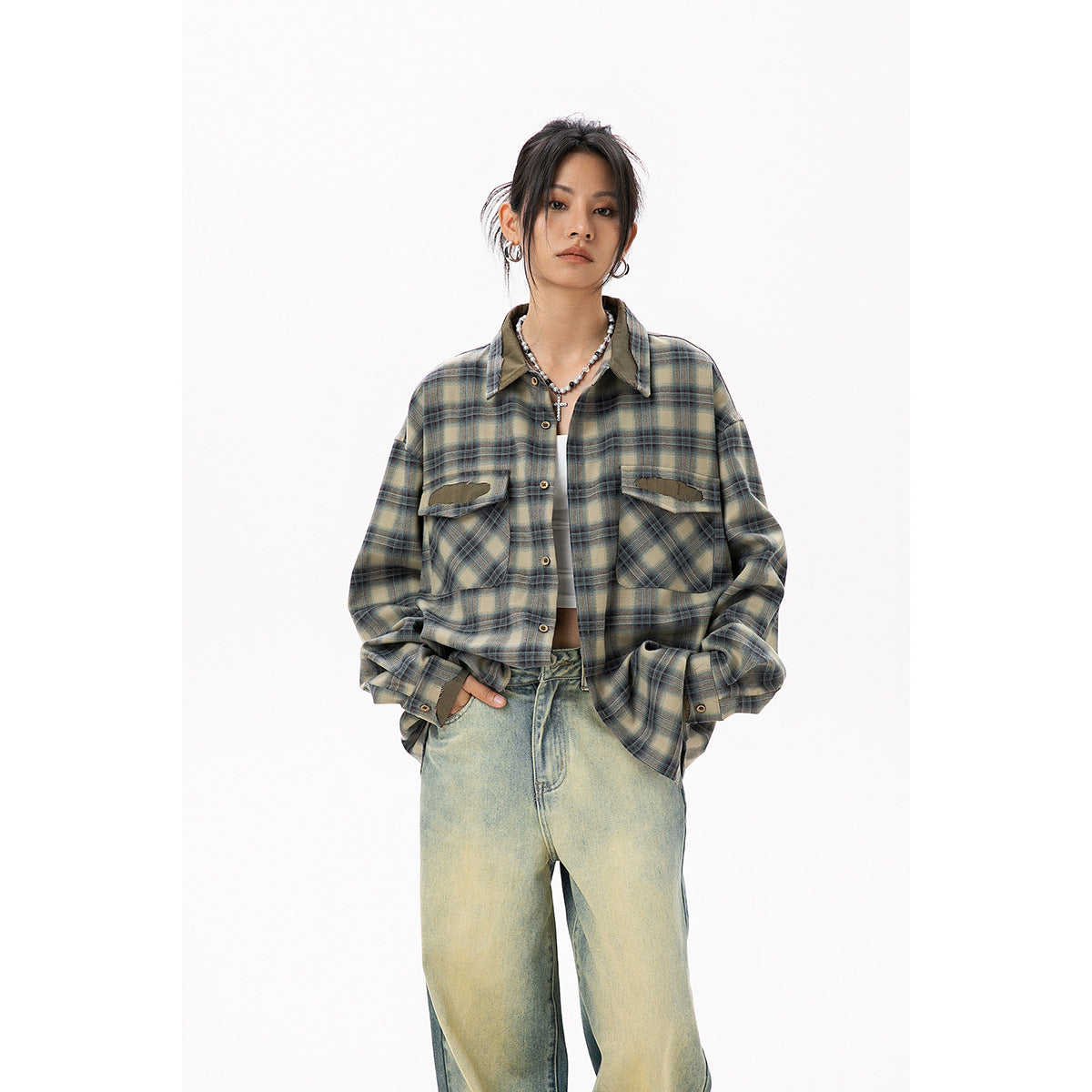 Front view of a model in an oversized olive and blue plaid shirt with large chest pockets and loose faded jeans.