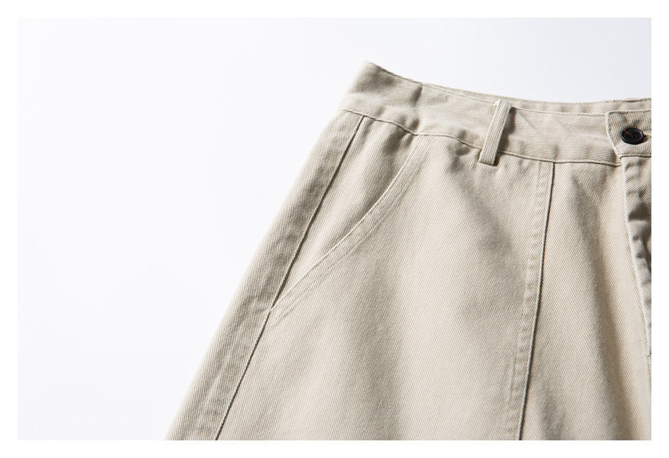 Close-up of beige shorts waistband, belt loop, dark button and angled pocket seam.