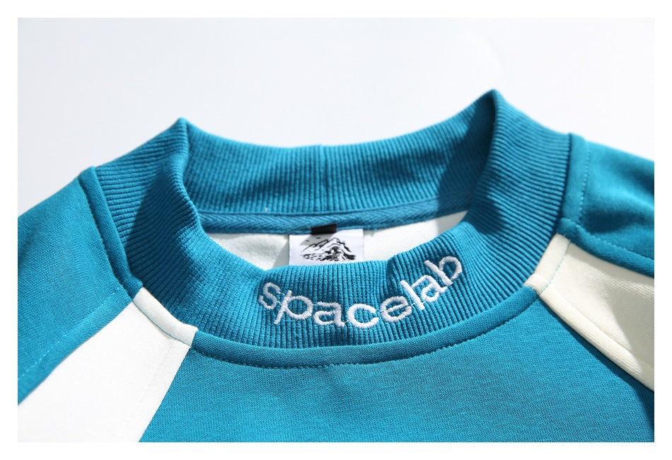 Close-up of the teal sweatshirt's ribbed collar with white embroidered lettering and cream shoulder panels.