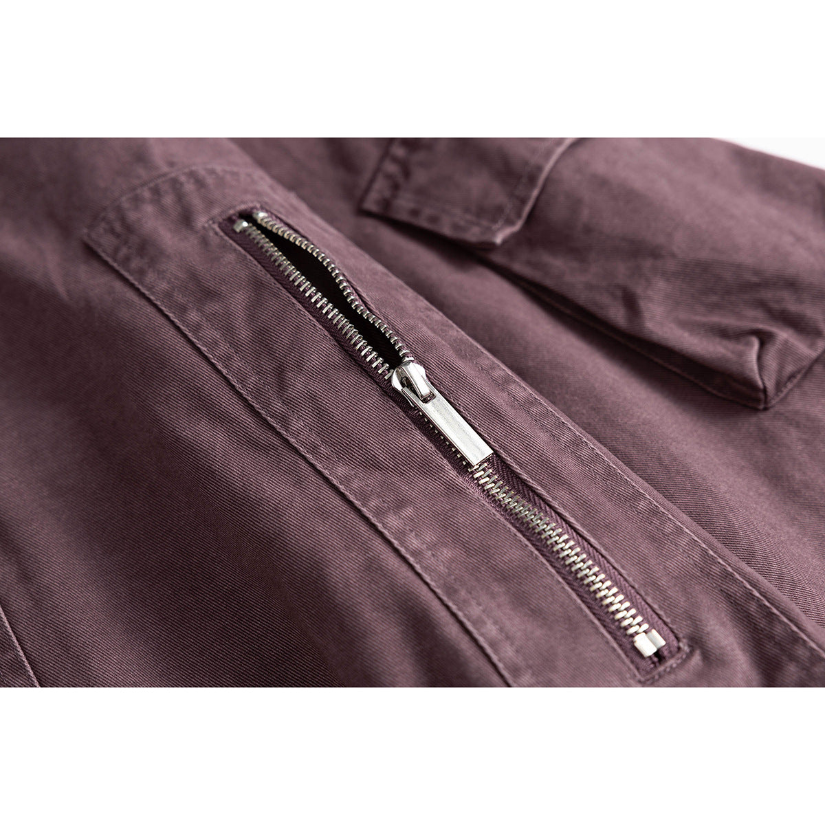 Close-up of a metal zip pocket and stitched flap pocket on a plum jacket.