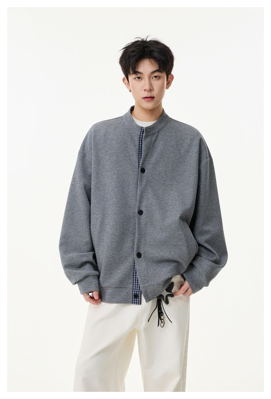 Model wears an oversized gray button-front jacket with a stand collar and checked placket over white trousers.