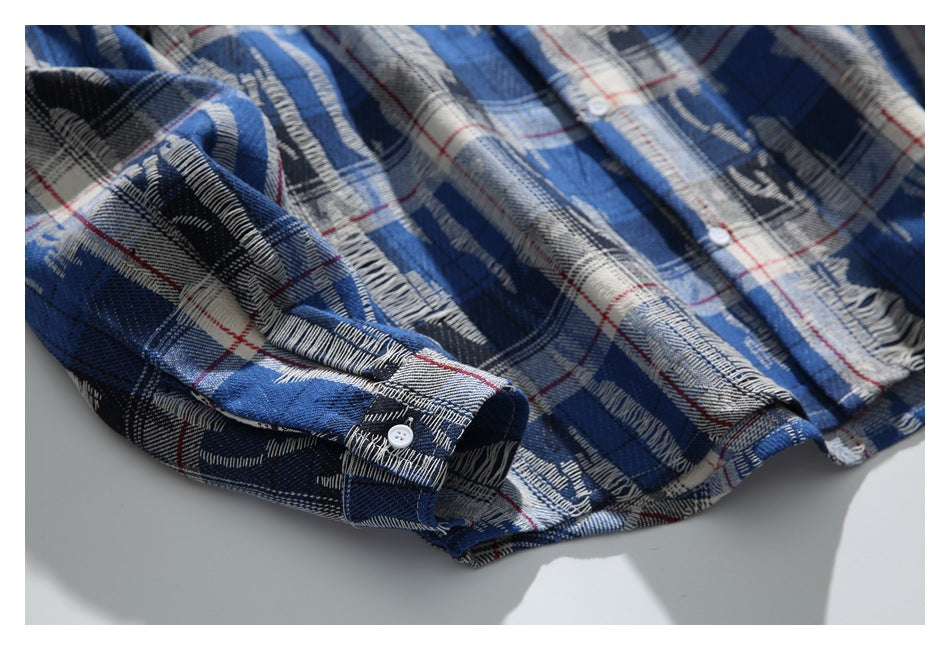 Close-up of a blue, black, and cream plaid shirt with thin red lines and a white button at the cuff.