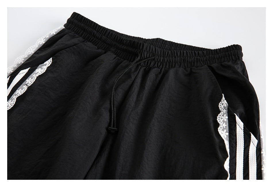Close-up of black pants with an elastic drawstring waist and white striped, floral-lace side trim.