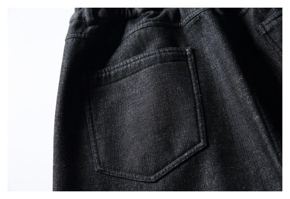 Close-up of a stitched patch pocket on the back of black textured trousers.
