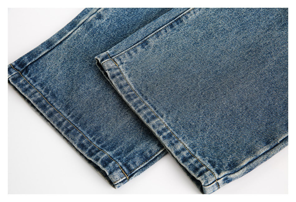 Close-up of blue denim jeans showing two folded leg hems and contrast stitching.