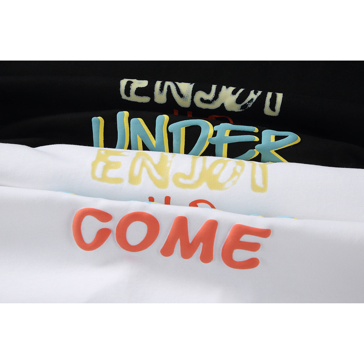 Close-up of black and white T-shirts with large colorful lettering, partly folded over one another.