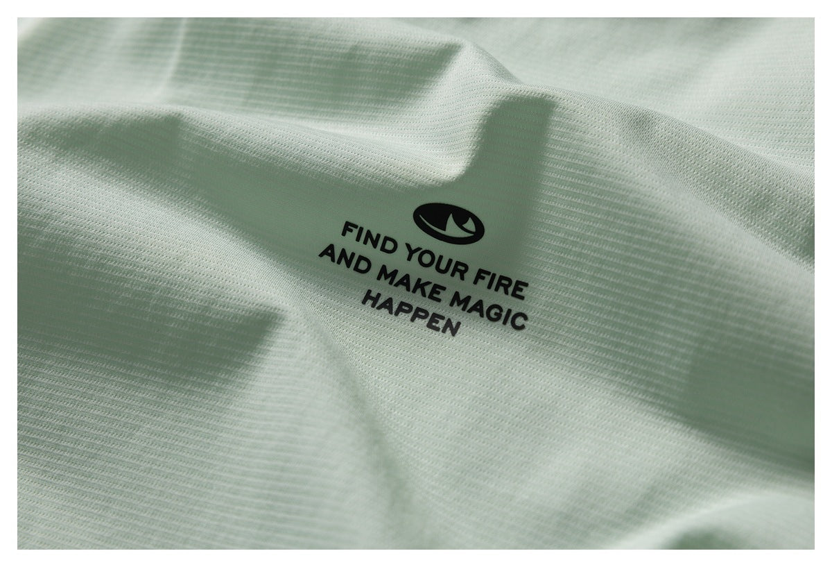 Close-up of pale mint-green knit fabric with a black logo and the slogan “Find Your Fire and Make Magic Happen.”