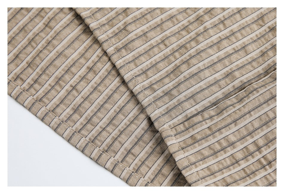 Close-up of overlapping striped tan shirt fabric and a stitched edge.
