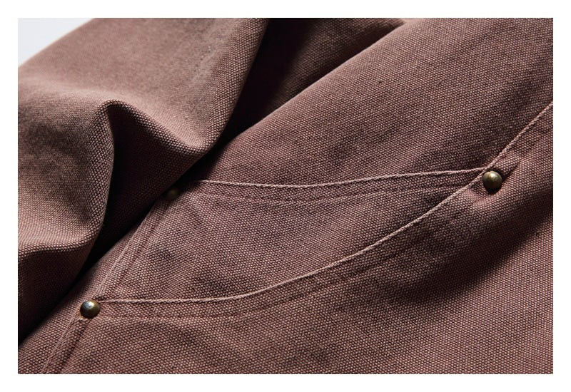 Close-up of a curved jacket pocket with double stitching and metal rivets on mauve-brown fabric.