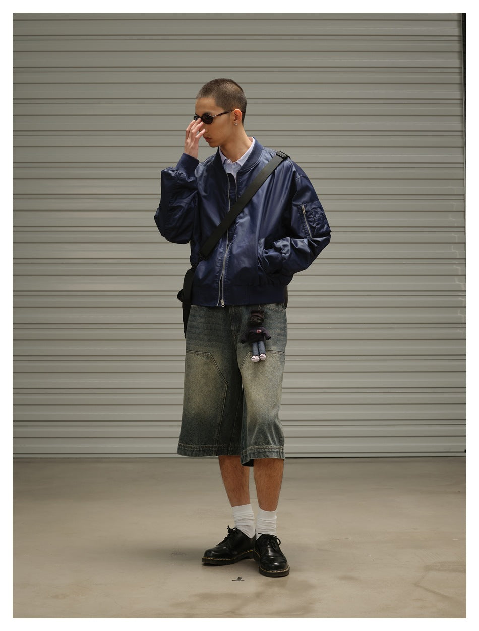 Model wearing a zipped navy bomber jacket with a black crossbody strap and oversized faded denim shorts.