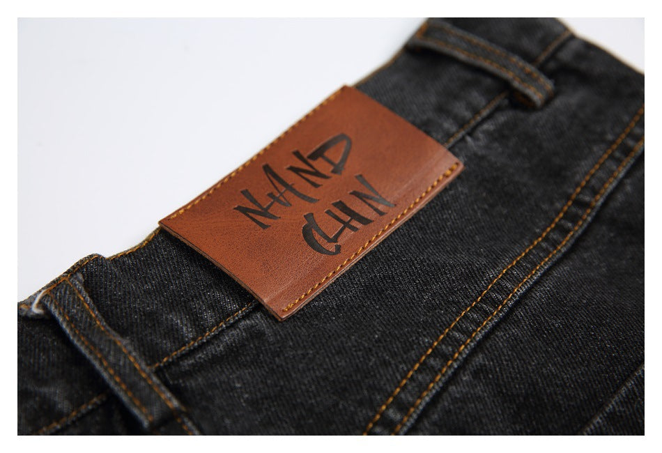 Close-up of a brown branded patch stitched onto the waistband of dark charcoal jeans.