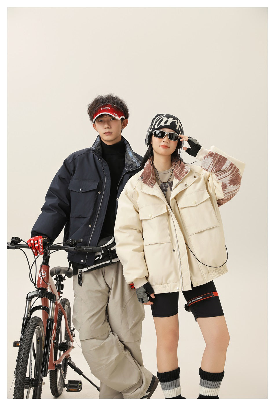 Two models pose beside bicycles wearing a dark navy jacket and a cream jacket with patterned panels.