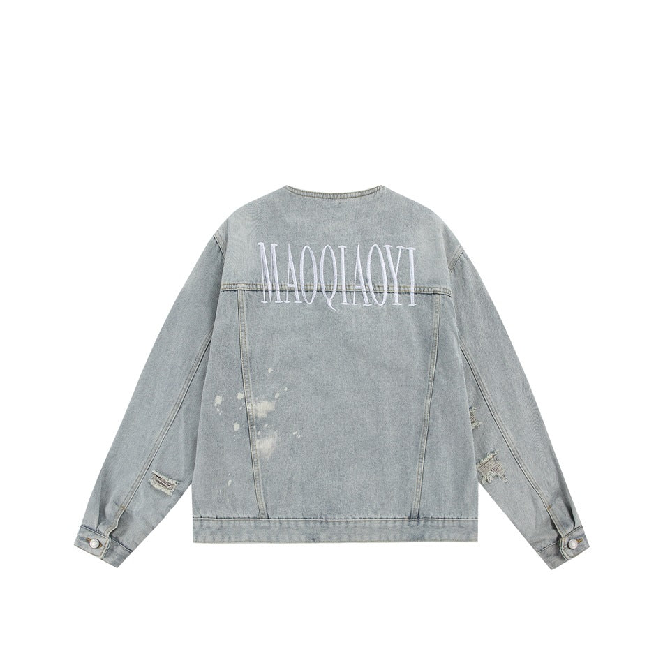 Back view of a light-wash denim jacket with large white embroidered lettering and distressed sleeve details.