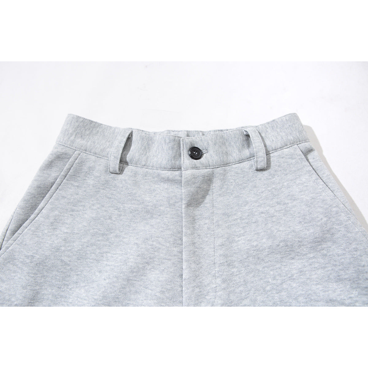 Close-up of light gray pants showing the front waistband, dark button, belt loops, and slanted pockets.