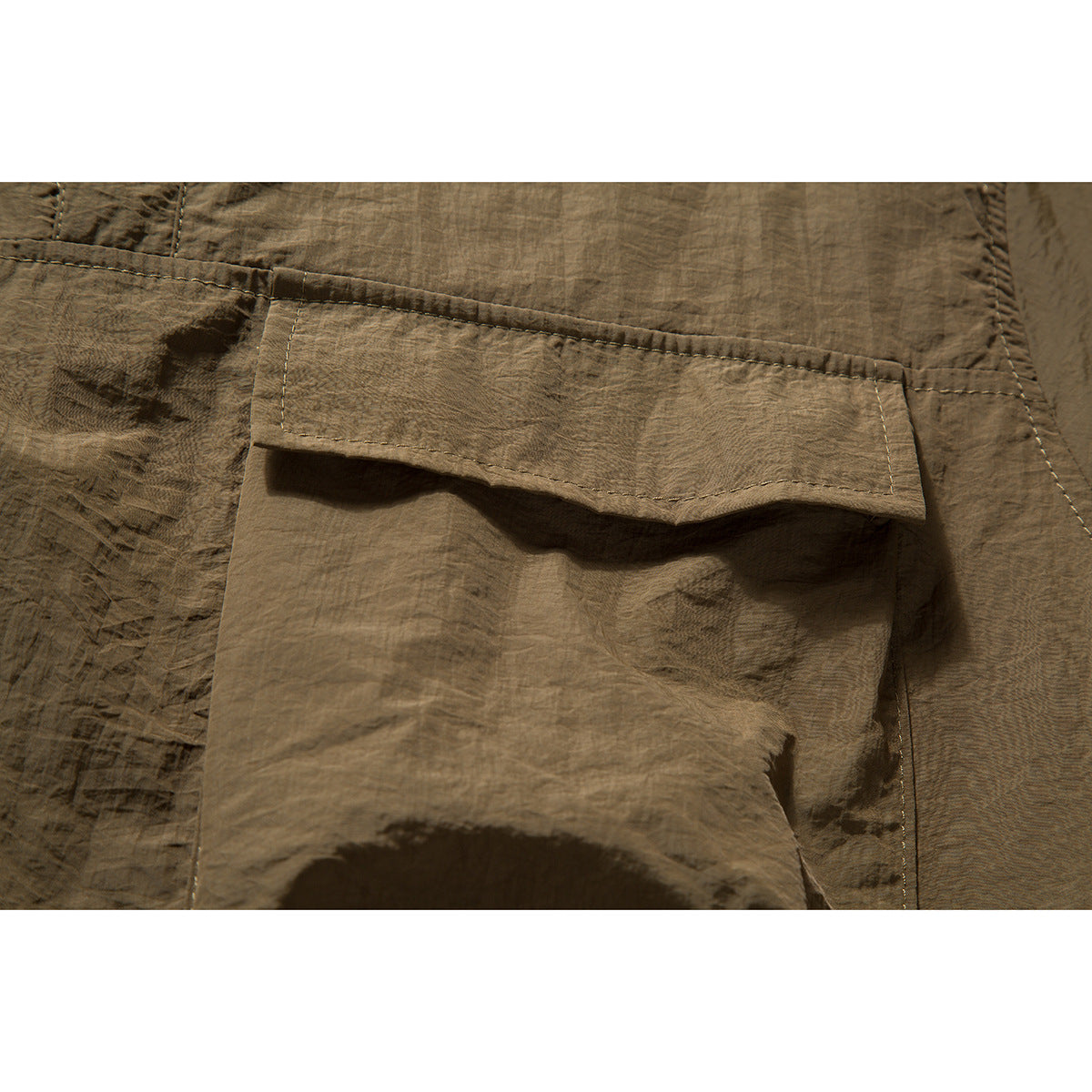 Close-up of an olive-brown shirt's large flap pocket and stitched seams.