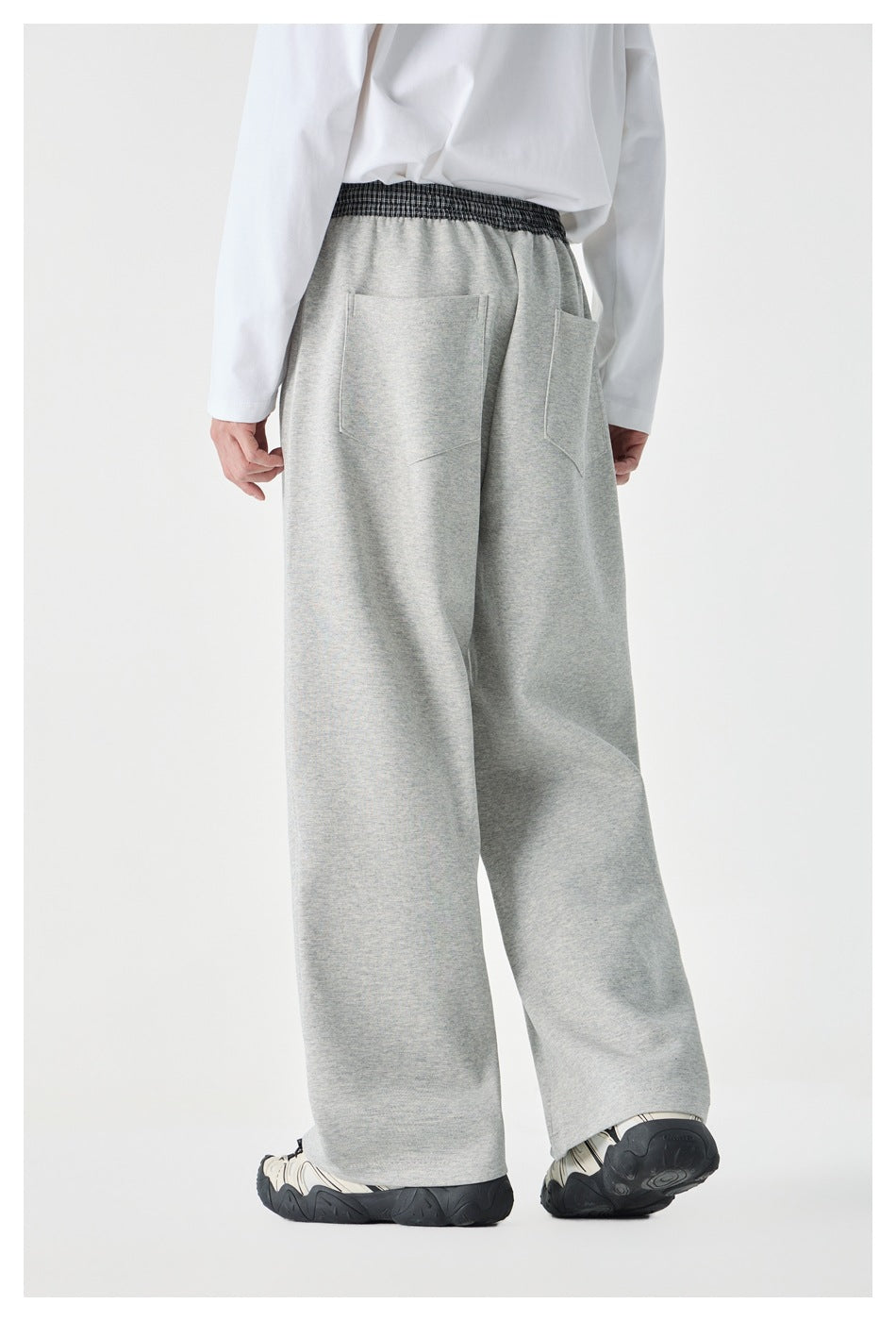 Rear view of a model wearing light gray wide-leg pants with a checked waistband and two back pockets.