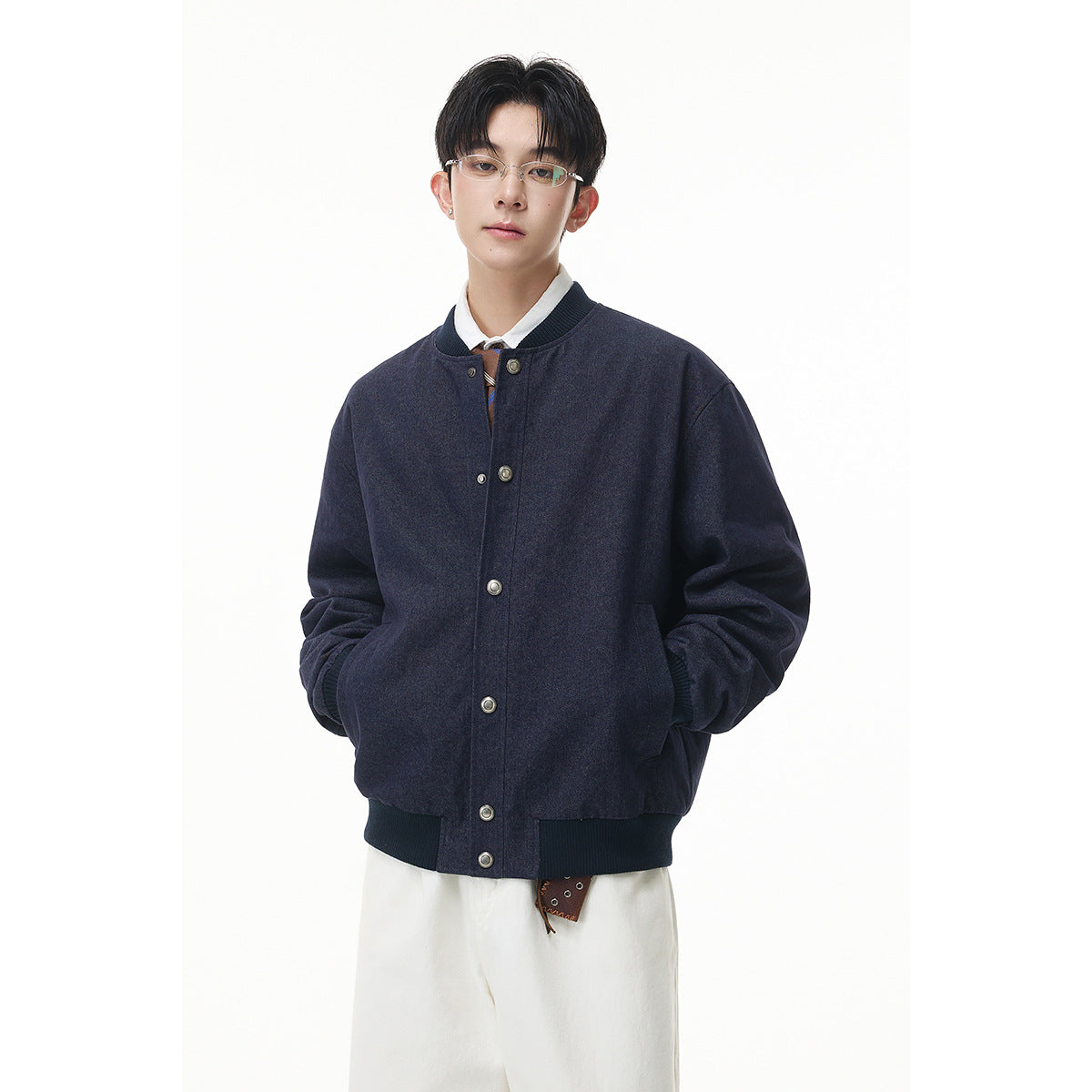 Model wearing a dark navy snap-front bomber jacket with ribbed collar, cuffs and hem, paired with white trousers.