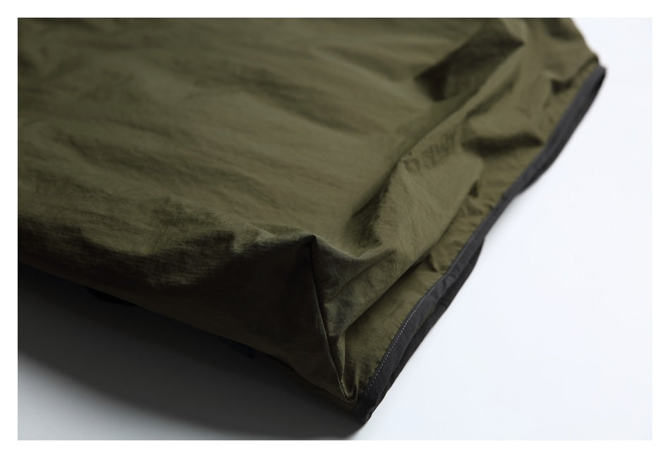 Close-up of the olive-green garment's hem with dark trim and stitched fabric folds.