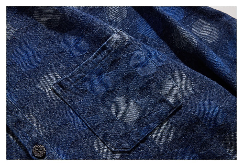 Close-up of a dark blue patterned shirt pocket, fabric, and dark button.