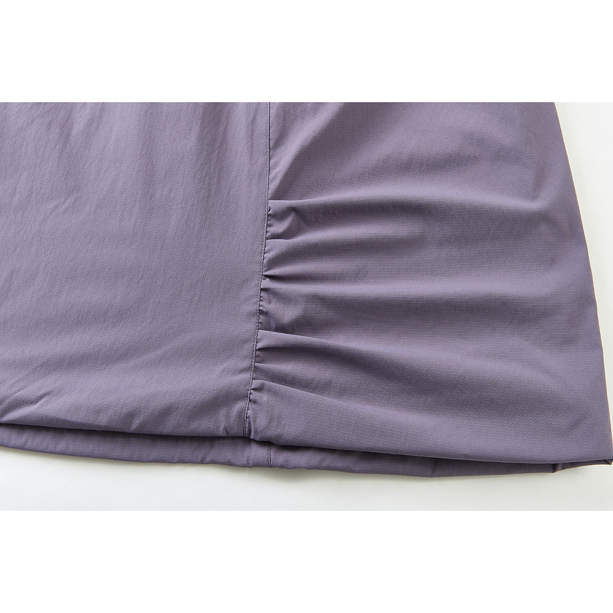 Close-up of a muted lavender skirt hem with a vertical gathered seam and stitching.