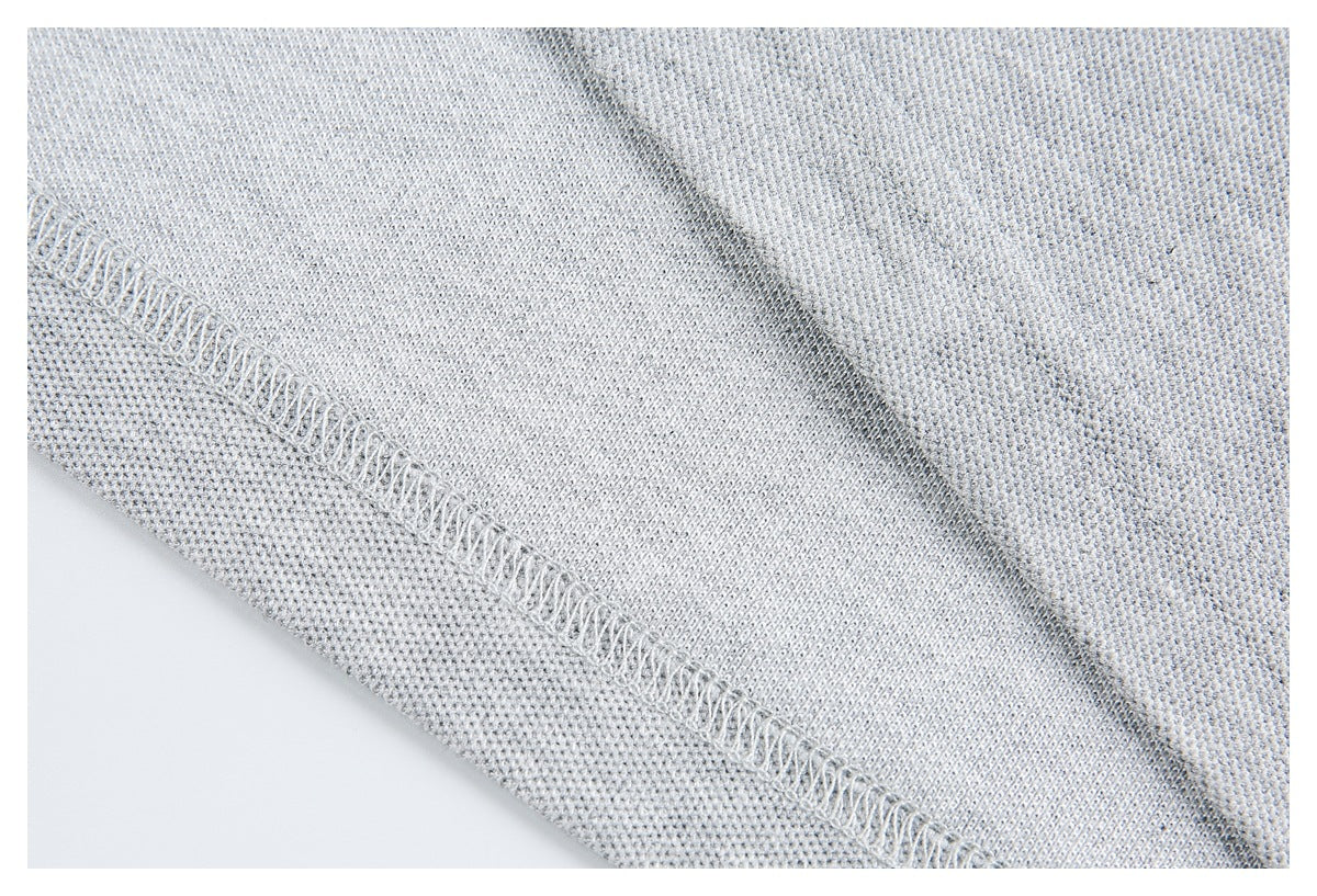 Close-up of light gray knit fabric with a diagonal overlock-stitched seam.