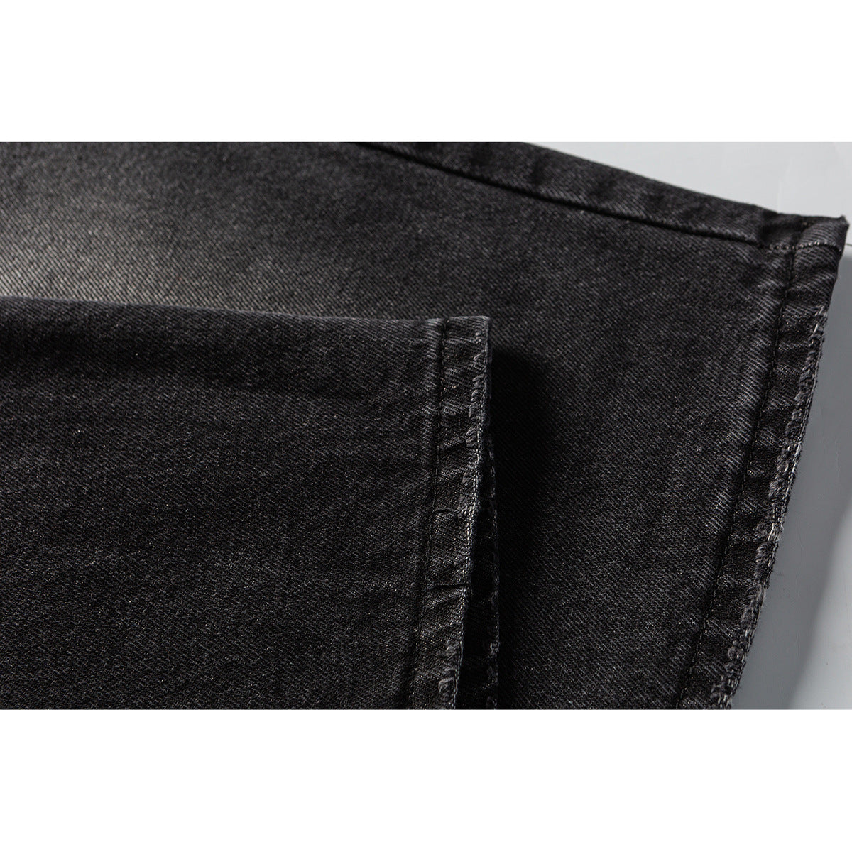 Close-up of black denim shorts showing a folded leg edge and stitched seam.