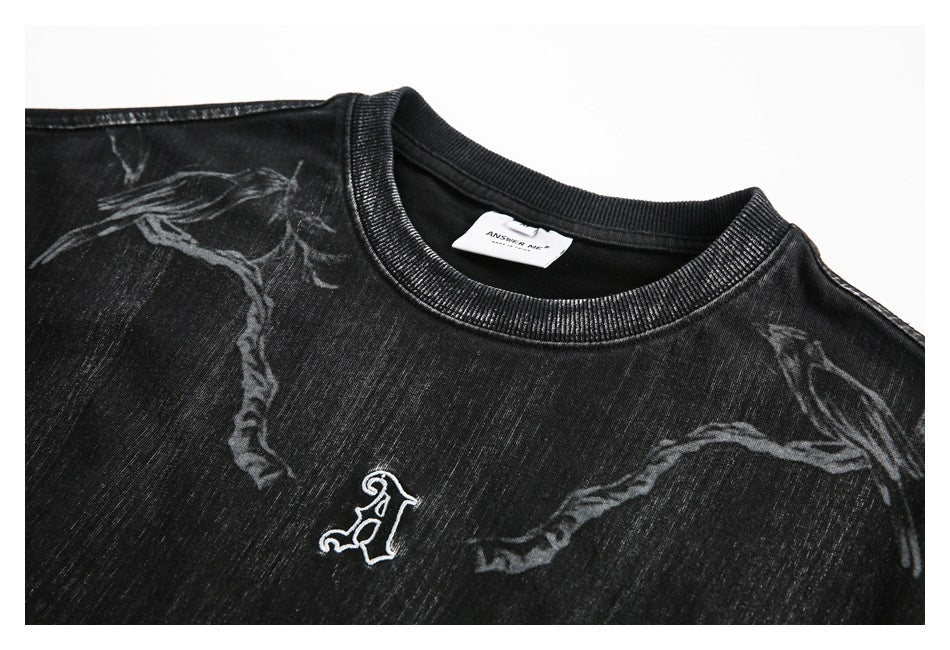 Close-up of a black shirt front with gray abstract graphics and a small white embroidered emblem.