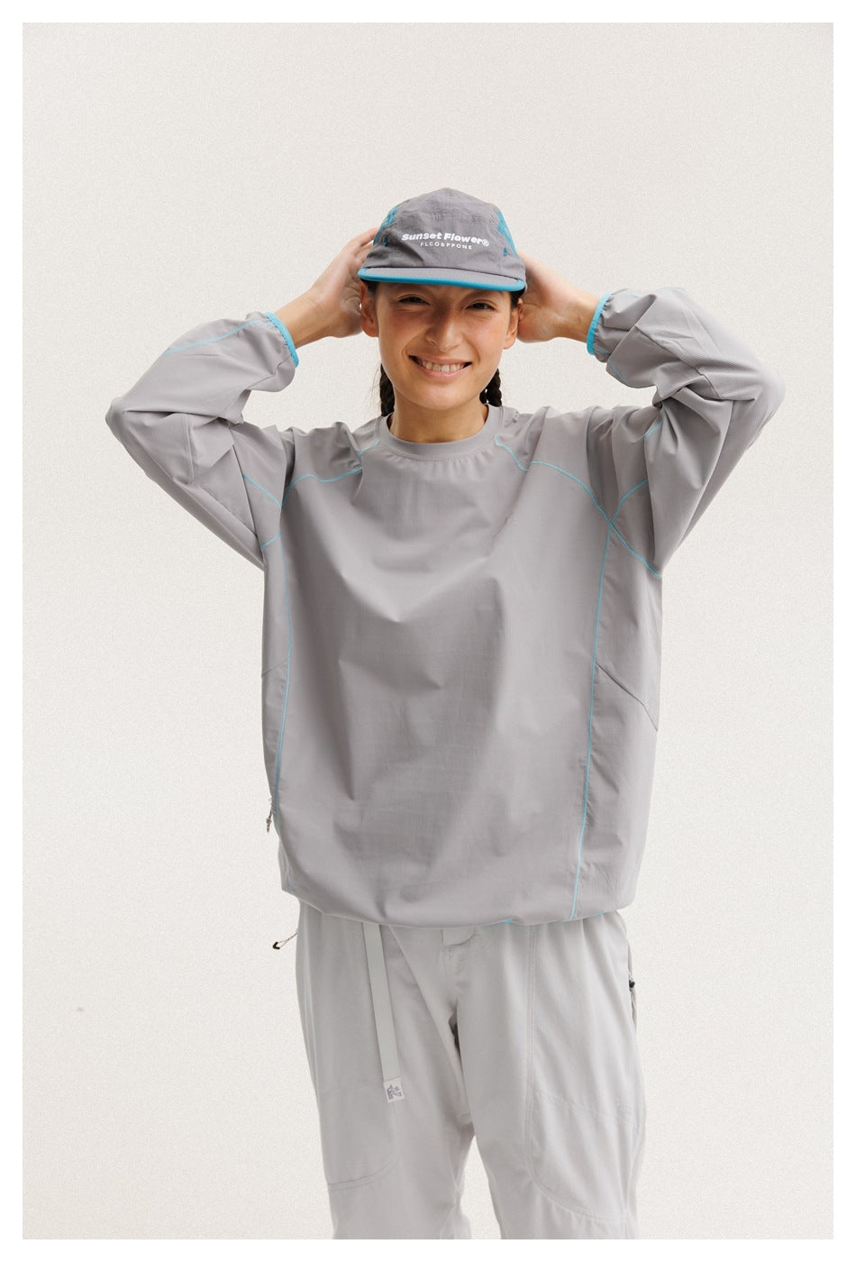 Closer front view of a model wearing a gray top with turquoise seam piping; a gray cap has white lettering.