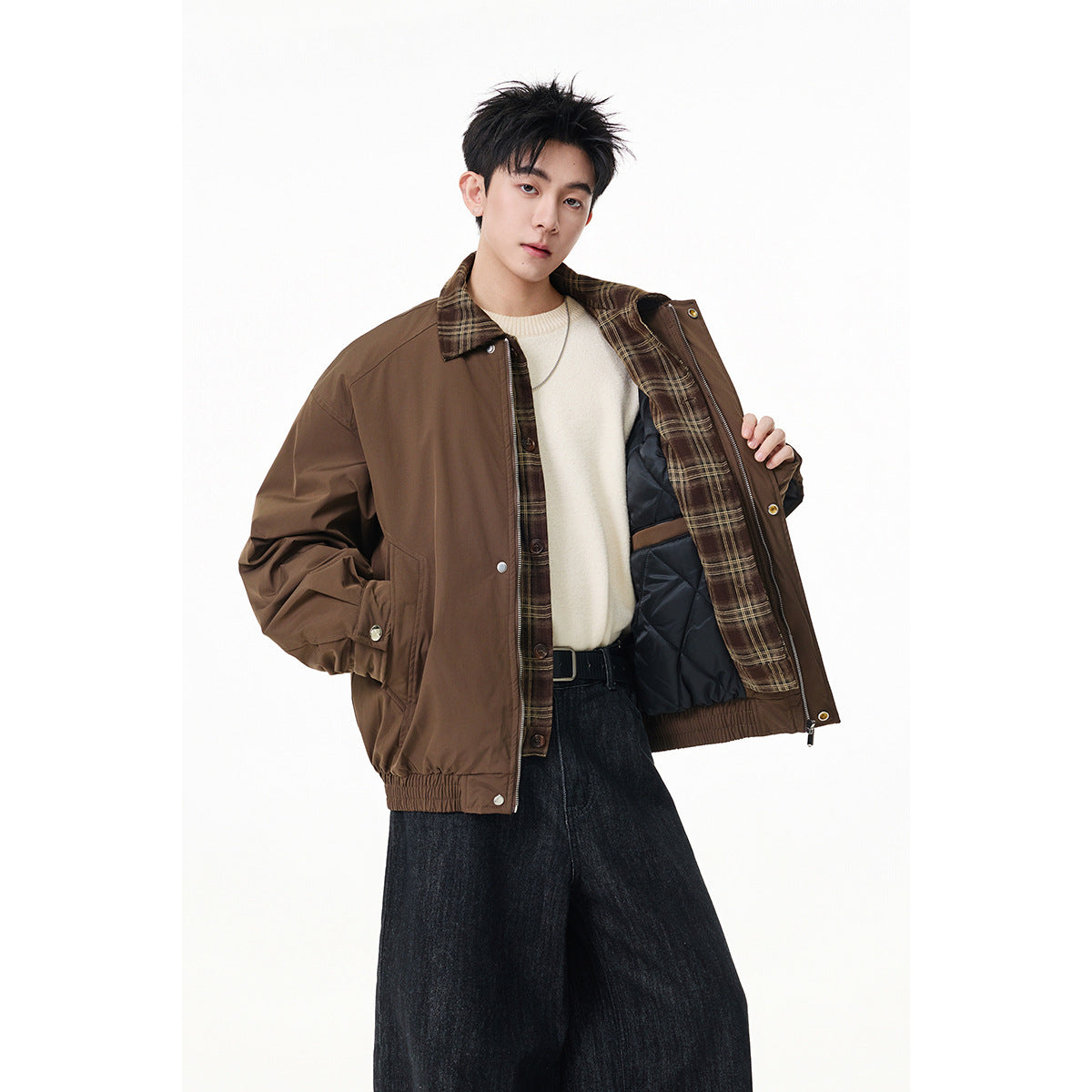 Model wearing an open brown jacket with plaid trim and dark quilted lining, paired with a cream sweater and wide dark jeans.