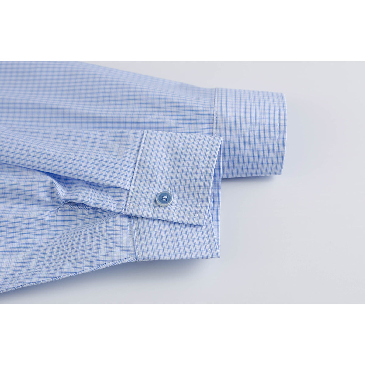 Close-up of the buttoned cuff on a light blue fine-check shirt.