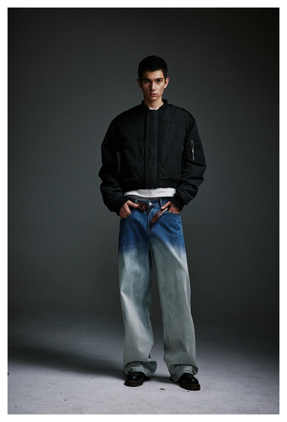 Front view of a model in a black bomber jacket, white shirt, very wide washed jeans and black shoes.