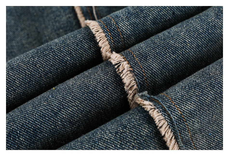 Close-up of dark indigo denim with orange stitching and frayed seam edges.