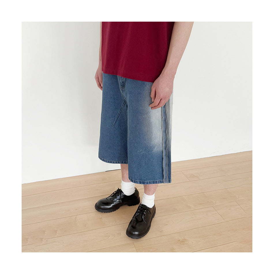 Side view of a model wearing faded blue denim shorts with raw-edge side seam detail, white socks and black shoes
