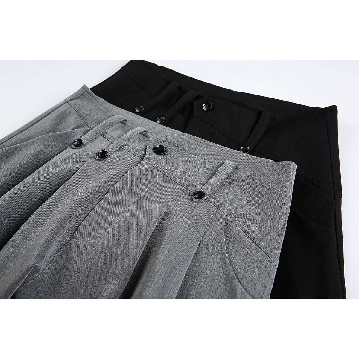 Close-up of gray and black trousers showing high waistbands, pleats, belt loops, and black buttons.
