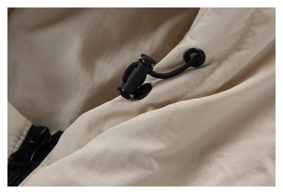 Close-up of a black elastic drawcord and stopper at the edge of the light beige jacket hood.