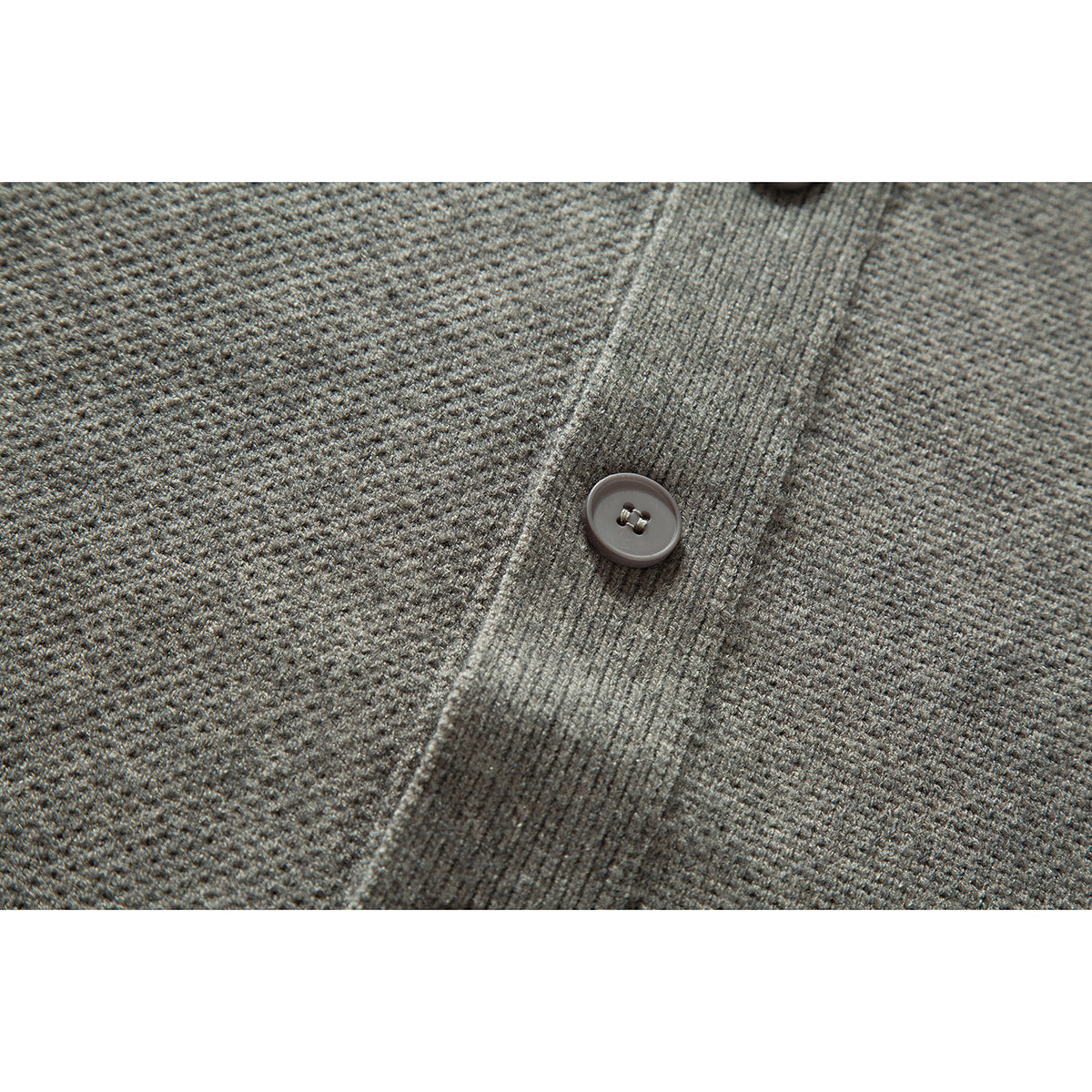 Close-up of a gray knit cardigan's textured fabric, button, and ribbed front placket.