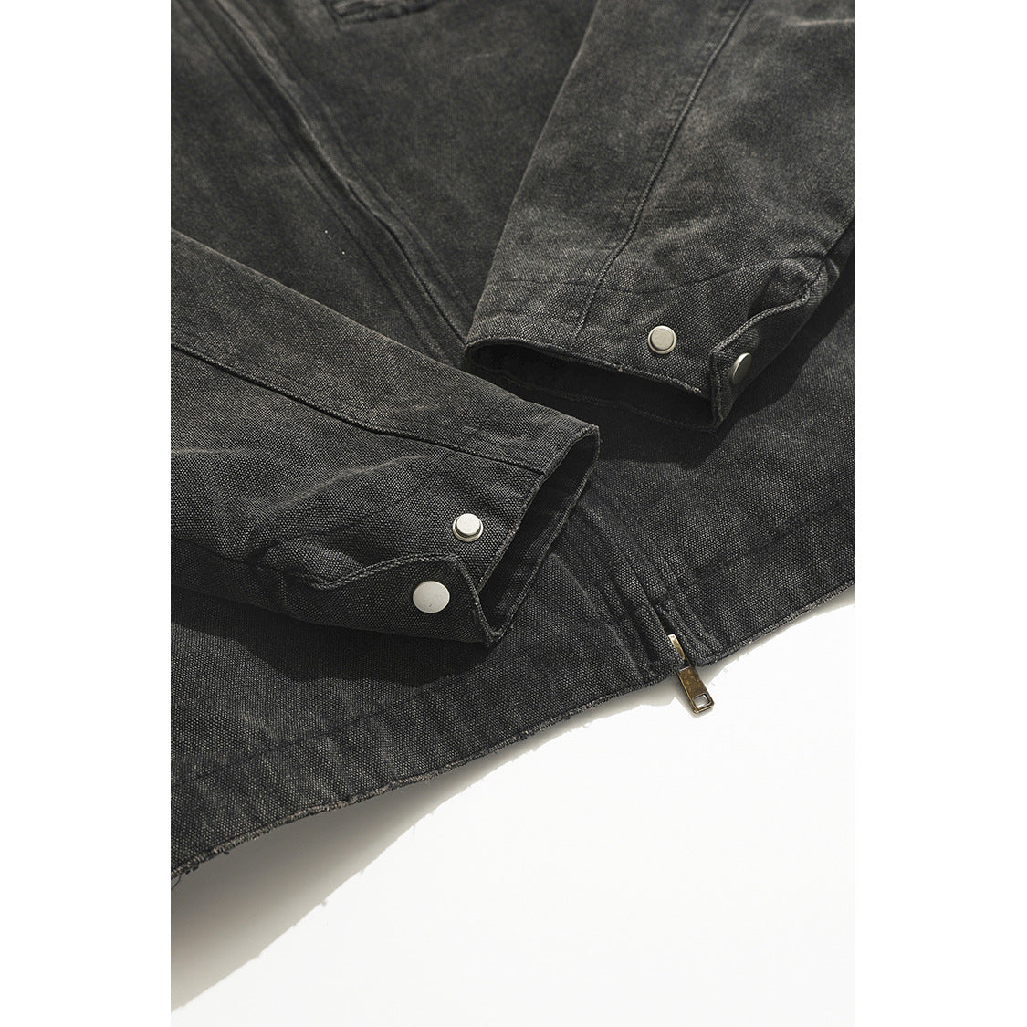 Close-up of a charcoal jacket’s snap-button cuffs and lower hem zipper.