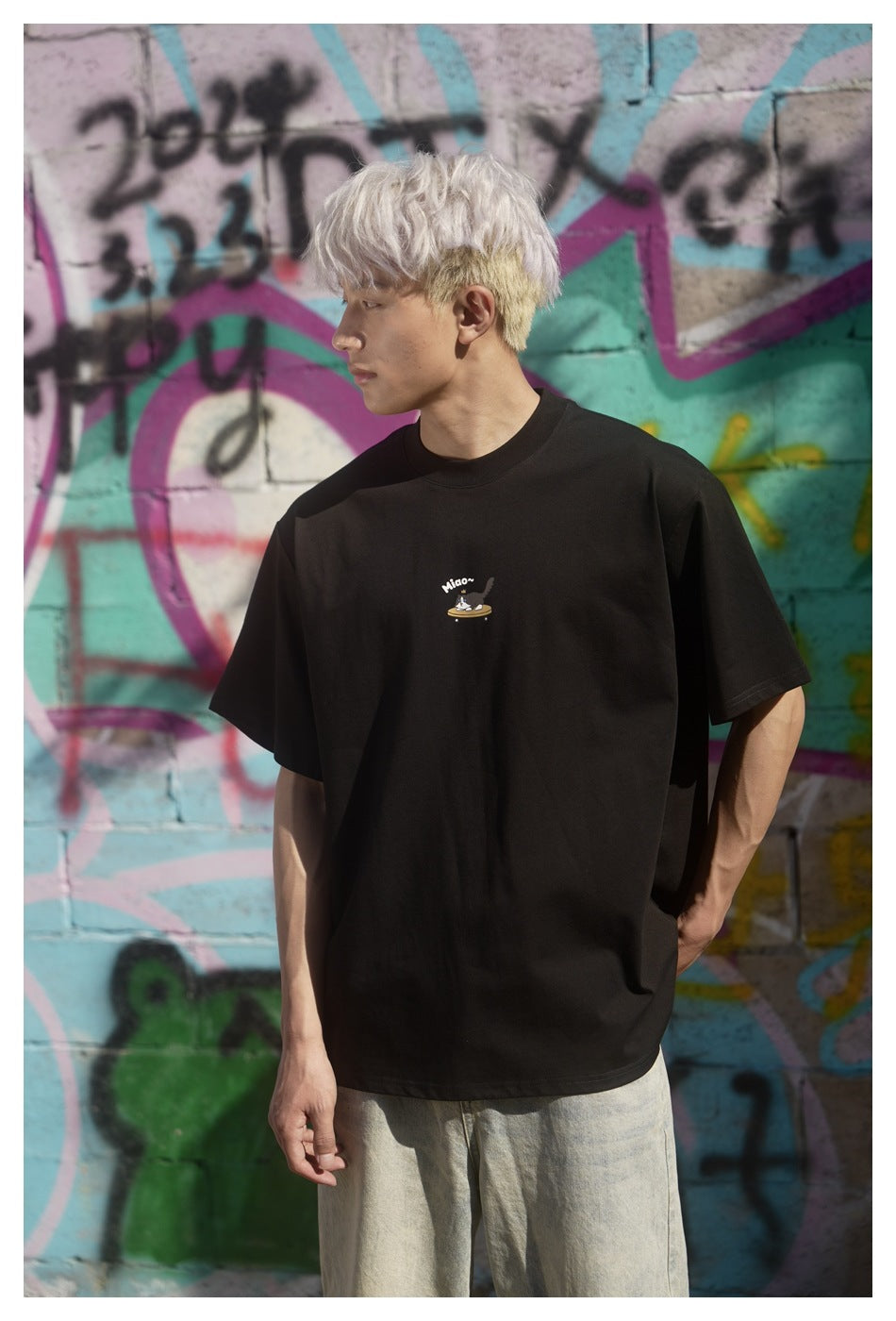 Front view of a model wearing a black oversized T-shirt with a small cat-on-skateboard chest graphic.