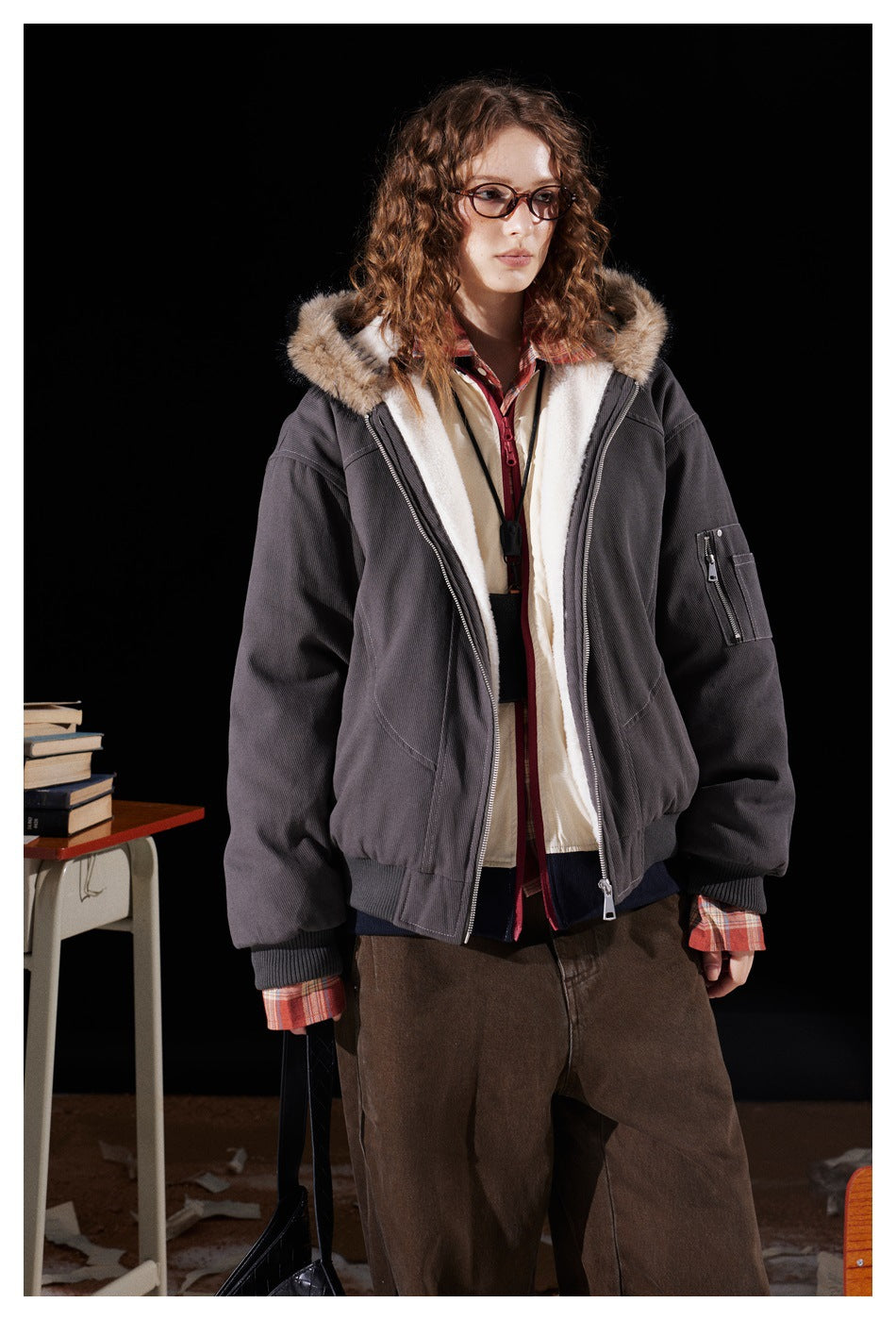 Model wearing open dark gray hooded jacket with fur-look hood trim and zippered sleeve pocket with brown pants
