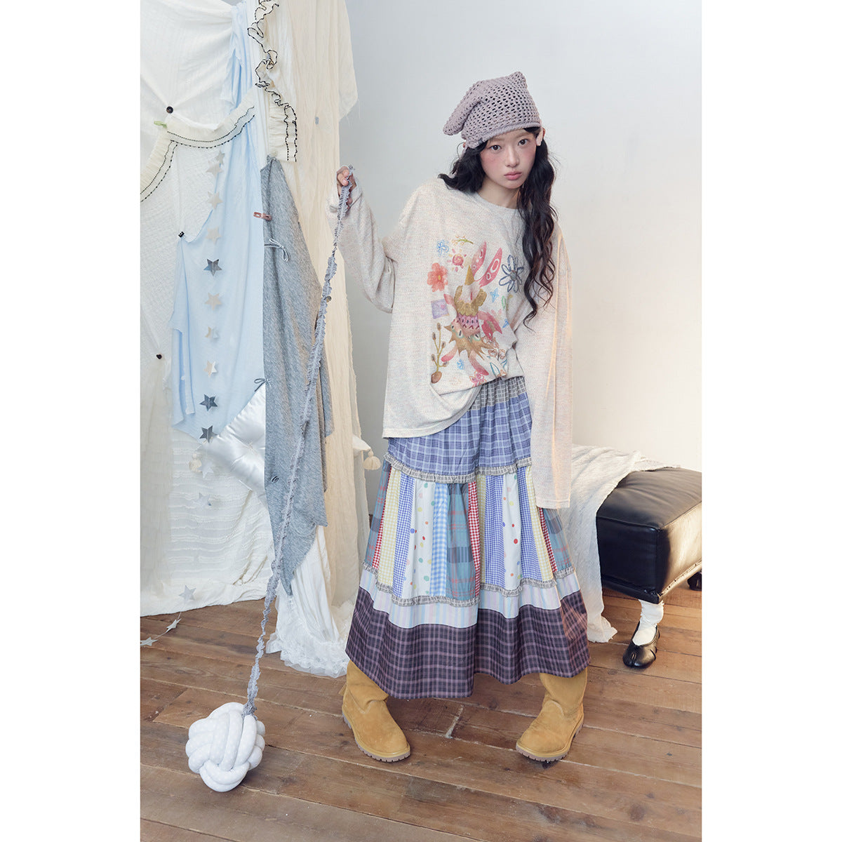 Model wearing a cream illustrated long-sleeve top and a colorful tiered patchwork skirt, holding a cord attached to a white