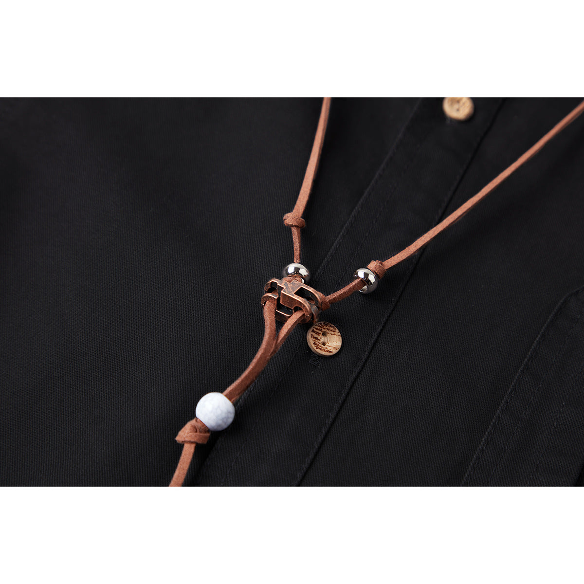 Close-up of a black shirt with a brown cord accessory, bead accents, and a tan button.