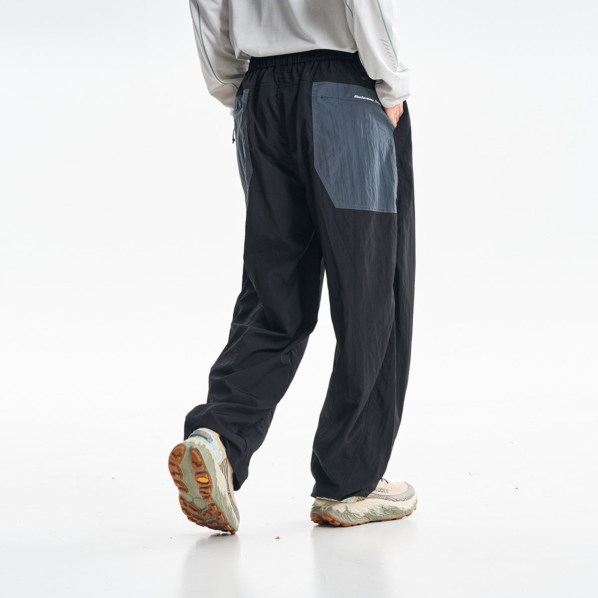 Rear view of a model wearing loose black pants with contrasting gray back pockets.