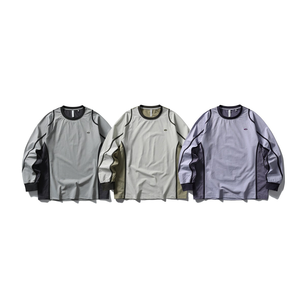 Three long-sleeve tops shown from the front in gray, cream, and lavender, each with dark contrast piping.