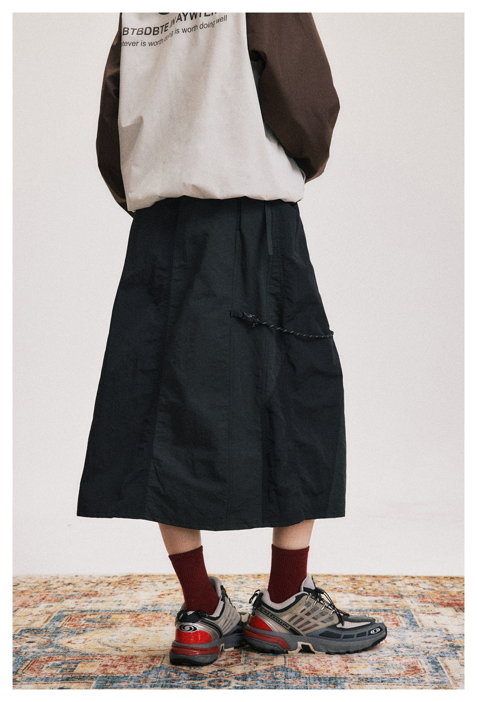 Rear view of a model wearing a black mid-calf skirt with a cord detail across the back.