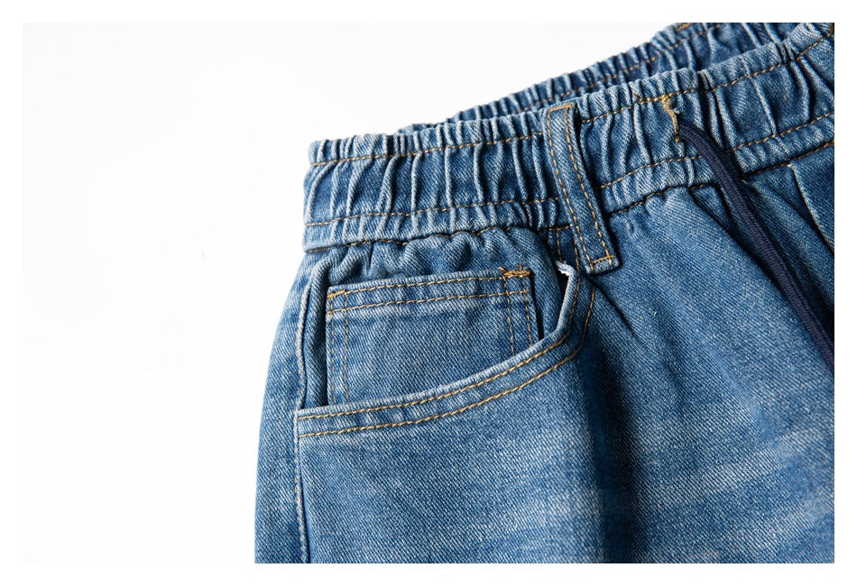 Close-up of blue denim pants showing an elastic waistband, belt loop, drawstring, and front pocket.